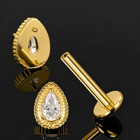 Labret tytanowy Hindu Drop Crystal – złote PVD, ASTM F-136 Labret do piercingu z ozdobnym topem w kształcie gruszki, ozdobionym białą cyrkonią osadzoną wewnątrz dekoracyjnej oprawy o karbowanym wykończeniu.
