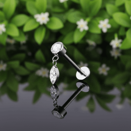 labret z zawieszką . Nakrętka labreta składa się z okrągłej, białej cyrkonii o średnicy 3 mm z której zwisa delikatny łańcuszek, zakończony cyrkonią o wydłużonym kształcie markizy (5 mm).